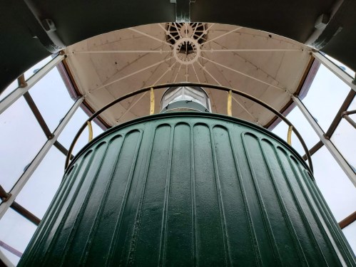 View from inside a lighthouse, looking up at the lantern room and ceiling through glass windows.
