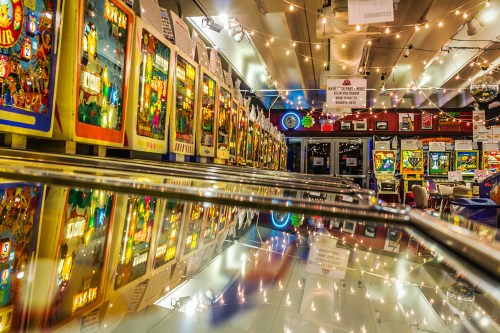 A vibrant arcade filled with vintage pinball machines, reflecting lights and colorful artwork on the glass surfaces.