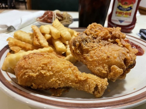 A plate of crispy fried chicken with crinkle-cut fries and a side of ketchup.