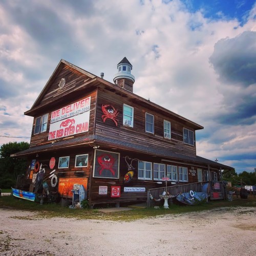 A rustic wooden building with a lighthouse feature, featuring signs for "The Red Eyed Crab" and various nautical decorations.