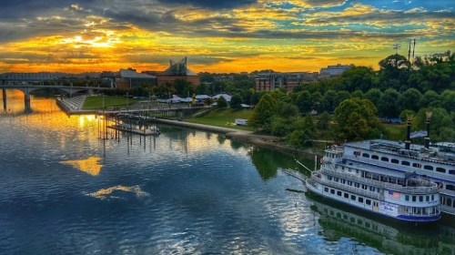 A scenic view of a river at sunset, with a boat docked and lush greenery along the shore.