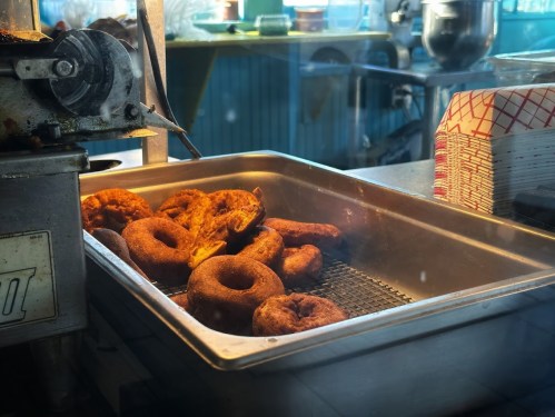 Freshly fried donuts cooling in a metal tray, with steam rising in a bright kitchen setting.