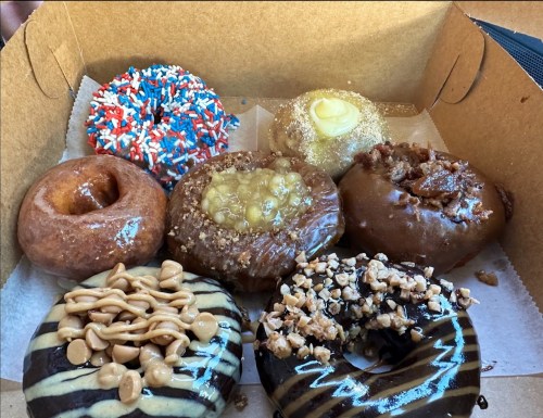 A box of assorted donuts, featuring various toppings like sprinkles, caramel, nuts, and chocolate glaze.