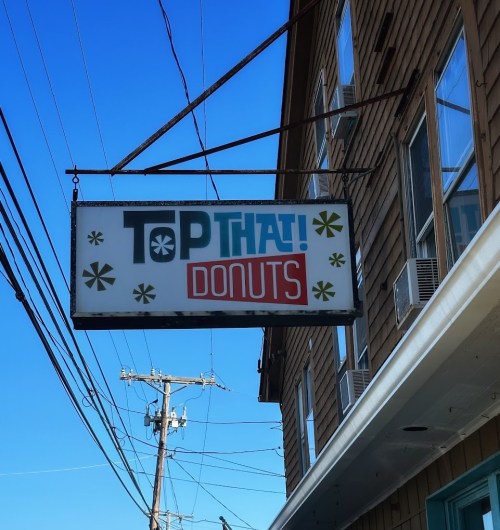 Sign for "Top That! Donuts" hanging from a building against a clear blue sky.