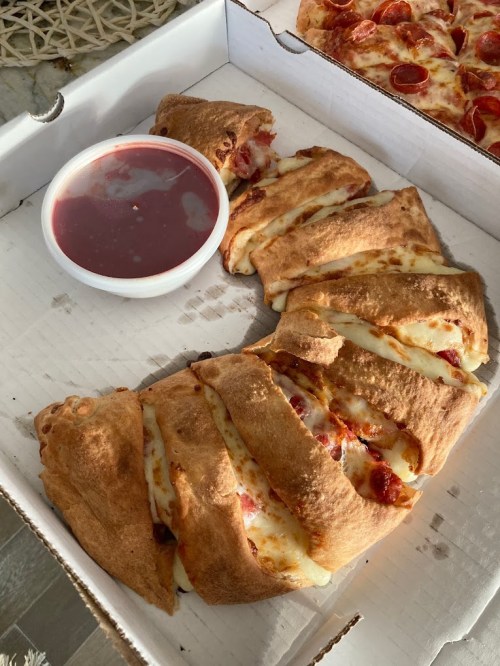 A pizza box containing a sliced pepperoni calzone and a small cup of marinara sauce.