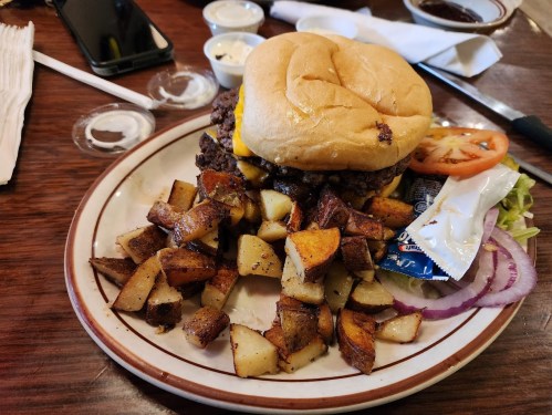 A juicy cheeseburger with lettuce, tomato, and onion, served with crispy potato wedges on a plate.