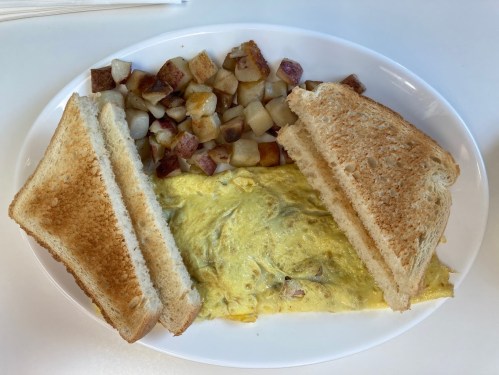 A plate with a fluffy omelet, toasted bread, and a side of diced, golden-brown potatoes.