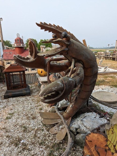 A large, whimsical metal sculpture of a lobster with exaggerated features, set in an outdoor art space.