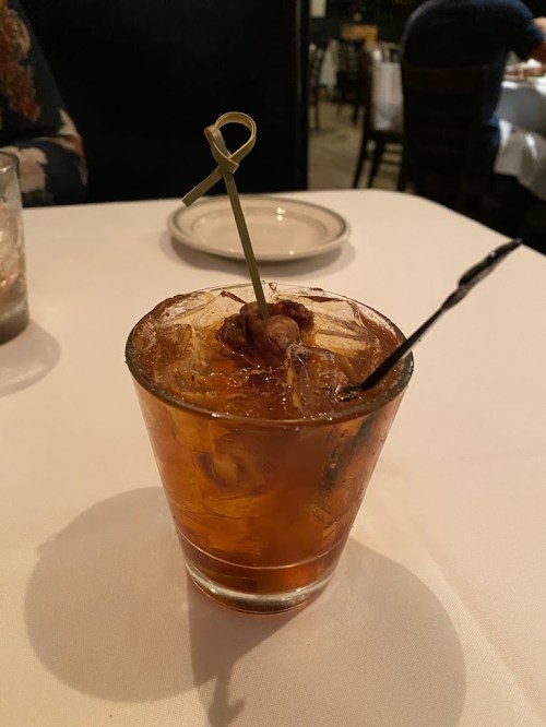 A glass of iced cocktail with a garnish, served on a white tablecloth in a restaurant setting.