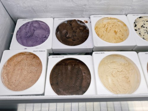 A variety of ice cream flavors in containers, including chocolate, vanilla, and fruity pebbles, displayed in a freezer.