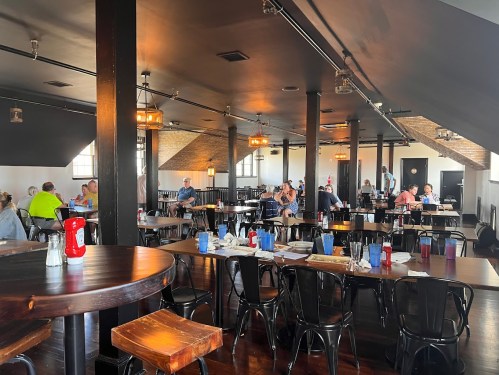 A spacious restaurant interior with diners at tables, featuring wooden beams and casual decor.