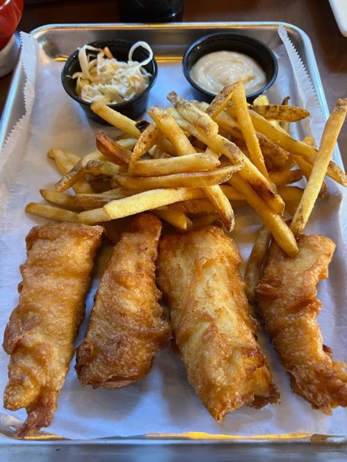 A tray with four pieces of golden fried fish, a side of fries, and two small bowls of coleslaw and dipping sauce.