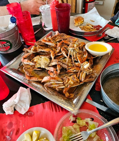 A platter of cooked crabs with melted butter, surrounded by plates of salad and fries at a casual dining table.
