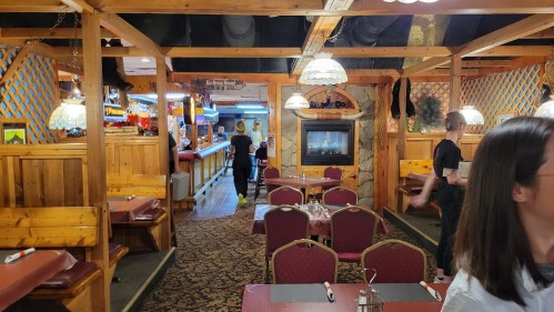 Interior of a cozy restaurant with wooden decor, tables set for dining, and a bar area in the background.