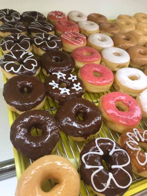 A variety of colorful donuts arranged on a tray, featuring chocolate, pink, and glazed options with decorative icing.