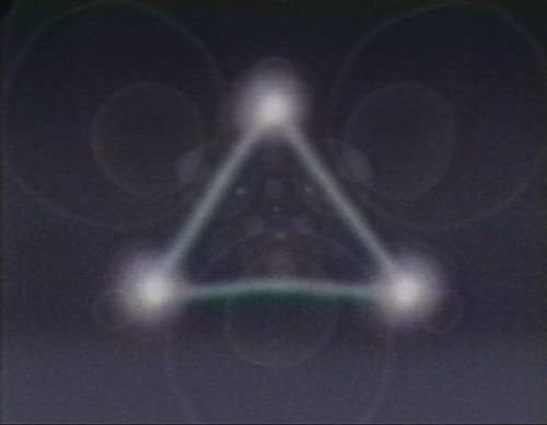 Abstract image featuring a blurred triangle with glowing points at each corner against a dark background.