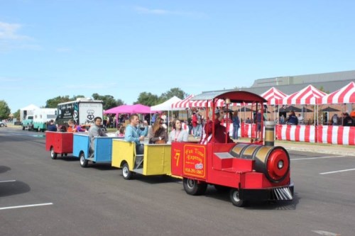 A colorful train ride with passengers enjoying a festive outdoor event under a clear blue sky.