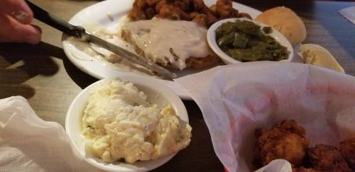 A plate of comfort food featuring fried chicken, gravy, green beans, mashed potatoes, and a roll.