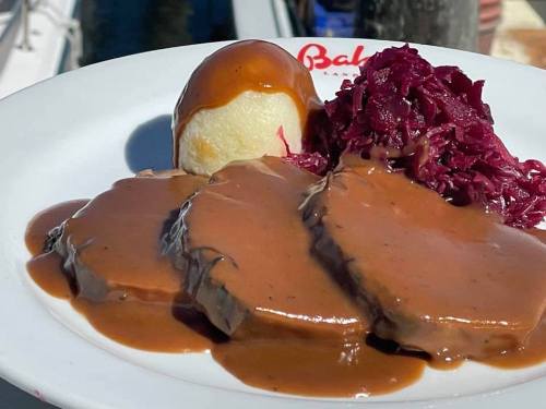 A plate of sliced beef in brown gravy, served with mashed potatoes and red cabbage.