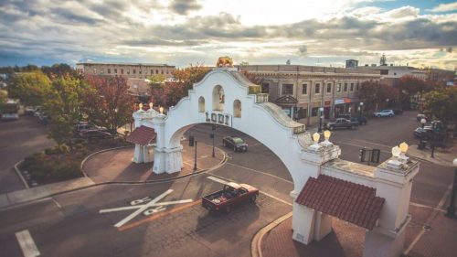Aerial view of the Lodi entrance arch, with shops and trees in the background under a cloudy sky.