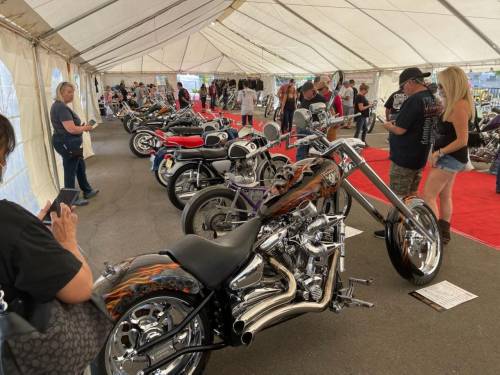 A motorcycle exhibition inside a tent, featuring various custom bikes and attendees admiring the displays.