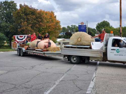 A truck towing a trailer with large pumpkins and people celebrating at a festive event.