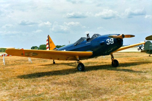 A vintage blue and yellow aircraft with the number 39 parked on a grassy field under a cloudy sky.