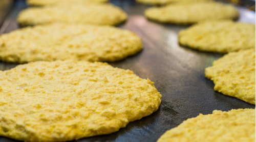Close-up of yellow corn tortillas cooking on a griddle, with a focus on their textured surface.