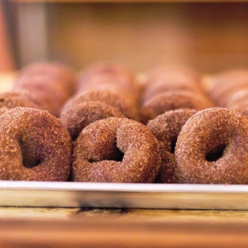 A close-up of freshly baked chocolate donuts coated in sugar, arranged neatly on a tray.