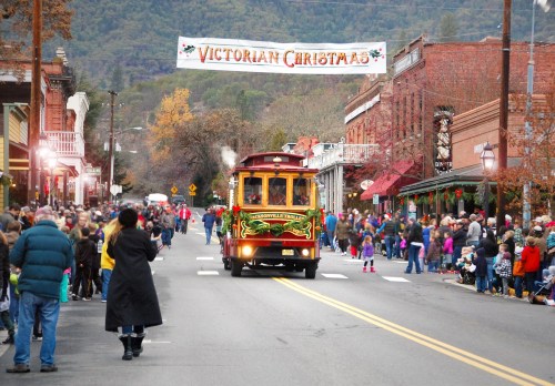 A festive street scene with a vintage trolley, crowds celebrating a Victorian Christmas in a charming town.