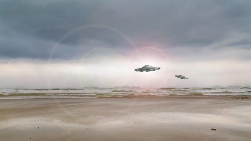 Two UFOs hover above a beach with dark, cloudy skies and gentle waves lapping at the shore.