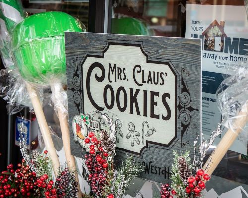 Sign for "Mrs. Claus Cookies" displayed in a festive window with candy and holiday decorations.