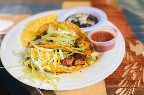 A plate of tacos with grilled chicken, lettuce, cheese, and salsa, served with rice and black beans on the side.