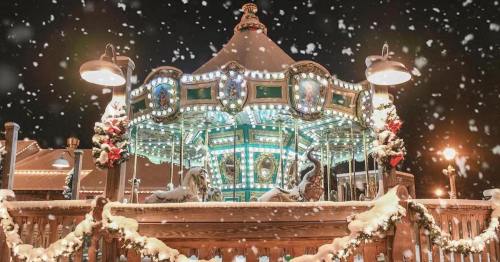A beautifully lit carousel adorned with festive decorations, surrounded by falling snow at night.