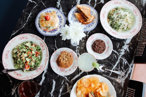 A table set with various dishes: salads, a sandwich, cookies, chips, and drinks, all on floral-patterned plates.