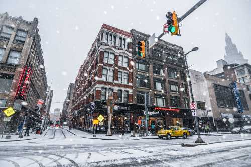 A snowy city street scene with a yellow taxi, traffic lights, and historic buildings in a winter setting.