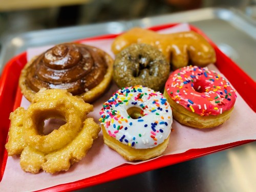 A red tray with a variety of donuts, including glazed, frosted, and a cinnamon roll, all on pink parchment paper.
