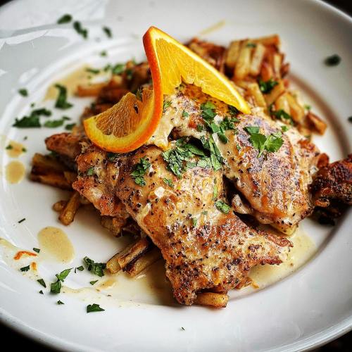 Grilled chicken topped with orange slices and herbs, served on a bed of crispy fries.