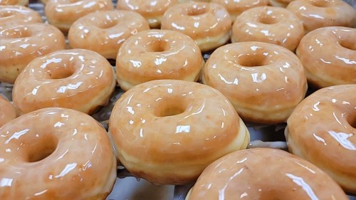 A close-up of freshly glazed donuts arranged in rows, showcasing their shiny, golden-brown surface.