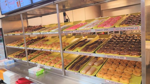 A display case filled with various donuts, including glazed, chocolate, and sprinkles, arranged on yellow trays.