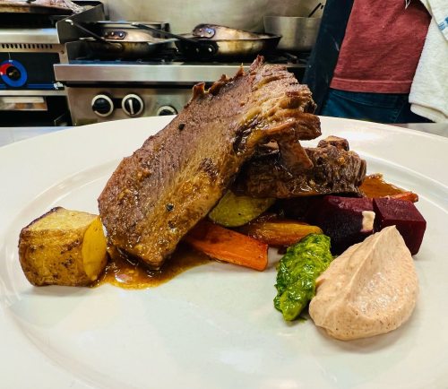 A plated dish featuring tender meat, colorful vegetables, and a creamy sauce, set in a kitchen environment.