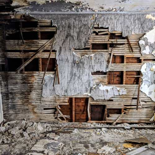 A dilapidated room with peeling walls, exposed wooden beams, and debris scattered on the floor.