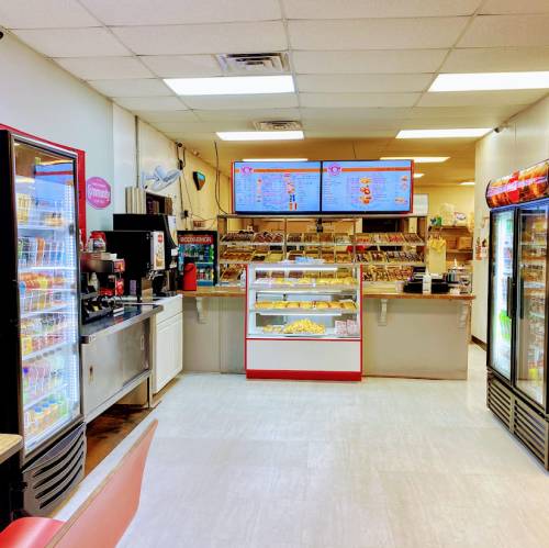 A bright convenience store interior with a display case of pastries, a menu board, and refrigerated drink shelves.
