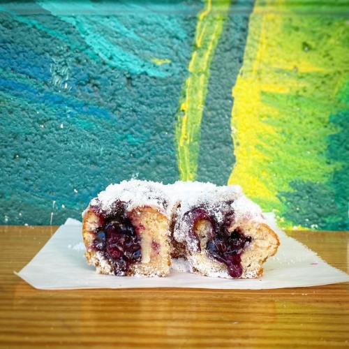 A sliced pastry filled with blueberries, dusted with powdered sugar, resting on parchment paper against a colorful background.