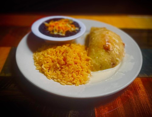 A plate of rice, a burrito, and a small bowl of black beans topped with cheese.
