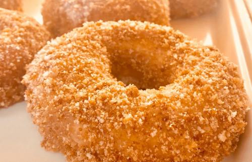 Close-up of a golden, crumb-coated donut with a glazed surface, resting on a white plate.