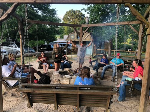 A group of people gathered around a fire pit, sitting on swings, enjoying a casual outdoor gathering.