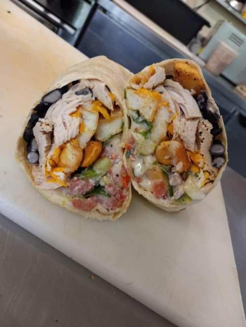 A cut burrito filled with chicken, black beans, cheese, tomatoes, and crunchy toppings, resting on a countertop.