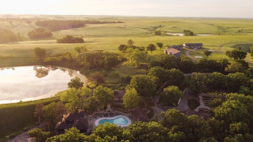 Aerial view of a serene landscape with a pool, lush greenery, and a pond surrounded by rolling hills.
