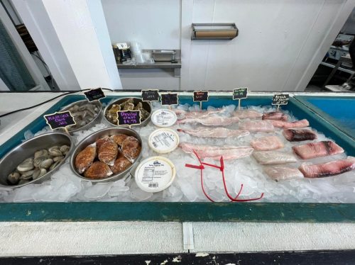 A seafood display featuring various fish fillets, shellfish, and prepared items on ice with price tags.